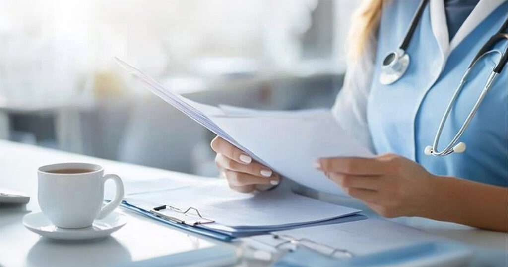 A healthcare billing specialist reviewing files alone at a desk, cup of tea beside them