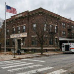 Older brick safety-net hospital with a faded sign and ambulance bay